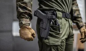 Osoba w mundurze taktycznym, z rękawiczkami Mechanix, prezentuje noszenie broni w kaburze na pasie.