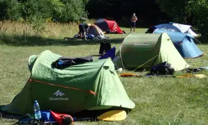 Zielony namiot Quechua, kilka innych rozstawionych na łące. Idealne miejsce, gdzie można rozbić namiot na dziko.