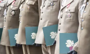 Żołnierze w mundurach z medalami odbierają dokumenty. Stare stopnie wojskowe zdobią ich piersi, a w rękach trzymają zielone teczki z godłem.