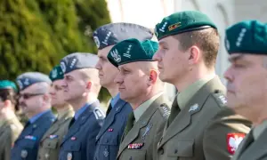 Żołnierze w różnych rodzajach mundurów wojskowych, w tym w zielonych beretach i szarych furażerkach, prezentują swoje odznaczenia i stopnie wojskowe.