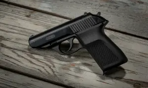 Czarny pistolet gazowy P.M.G.-23 leży na zniszczonej drewnianej desce. Do posiadania broni gazowej wymagane jest pozwolenie.