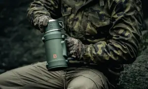 Osoba w mundurze maskującym trzyma duży, zielony termos. Pokazuje, jak wyczyścić nakrętkę od termosu, by napój pozostał świeży.