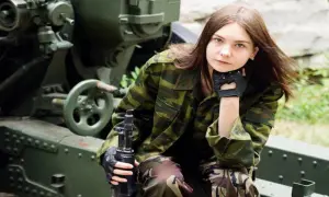 Młoda kobieta w mundurze wojskowym z karabinem obok działa. Zainteresowana tym, jak dostać się do wojska kobiecie?