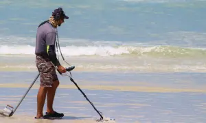 Mężczyzna z wykrywaczem metali na plaży. Czy wykrywacz metali jest legalny? Szuka skarbów w wodzie.