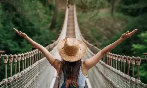 Kobieta w kapeluszu na moście wiszącym, z ramionami rozłożonymi w geście wolności. Przestrzega zasad "leave no trace", ciesząc się naturą.