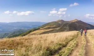 Piękny bieszczadzki krajobraz. Dwie osoby idą ścieżką przez trawiaste wzgórza w kierunku gór.