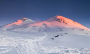 Elbrus, najwyższy szczyt w Europie, skąpany w różowym świetle wschodu słońca. Śnieżne zbocza usiane śladami nart.