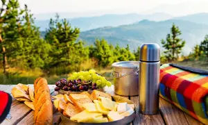 Piknik w górach: chleb, ser, winogrona, termos i kolorowy koc. Idealne jedzenie, by cieszyć się widokiem.