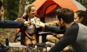 Grupa przyjaciół wznosi toast przy ognisku, ucząc się podstawowych zasad survivalu.