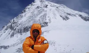 Alpinista w pomarańczowej kurtce na tle ośnieżonego szczytu. To może być jego wyczyn: mount everest bez tlenu.
