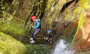 Dwóch mężczyzn w kaskach i piankach zjazdowych pokonuje wodospad w wąwozie. To właśnie jest canyoning!