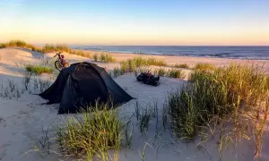Namiot i rower na plaży, idealne miejsce na spanie na dziko. Wschód słońca nad morzem.