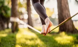 Chodzenie po taśmie to slackline. Widok na nogi balansujące na taśmie w parku, w promieniach słońca.