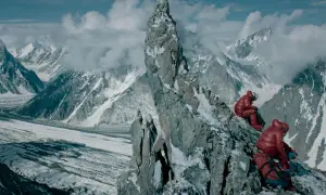 Wyprawa na Broad Peak 2013. Dwóch wspinaczy w czerwonych kurtkach odpoczywa na skalistym zboczu, podziwiając lodowce i ośnieżone szczyty.