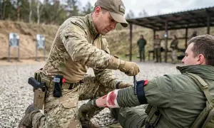 Żołnierz zakłada stazę taktyczną na ramię rannego kolegi na poligonie. To kluczowy element pierwszej pomocy.