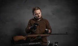 Mężczyzna w czarnych rękawiczkach przeprowadza konserwację wiatrówki, używając preparatu w sprayu i czyścika.
