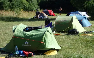 Zielony namiot Quechua, kilka innych rozstawionych na łące. Idealne miejsce, gdzie można rozbić namiot na dziko.