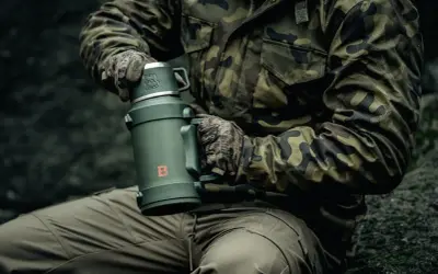 Osoba w mundurze maskującym trzyma duży, zielony termos. Pokazuje, jak wyczyścić nakrętkę od termosu, by napój pozostał świeży.