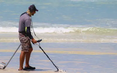 Mężczyzna z wykrywaczem metali na plaży. Czy wykrywacz metali jest legalny? Szuka skarbów w wodzie.