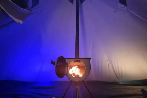 Piec w namiocie, płomienie tańczą w środku. Idealny sposób, jak ogrzać namiot zimową nocą.