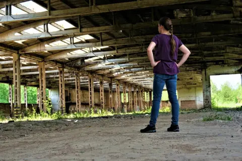 Dziewczyna w zrujnowanej hali, zastanawia się, czy urbex jest legalny.