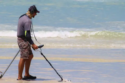 Mężczyzna z wykrywaczem metali na plaży. Czy wykrywacz metali jest legalny? Szuka skarbów w wodzie.