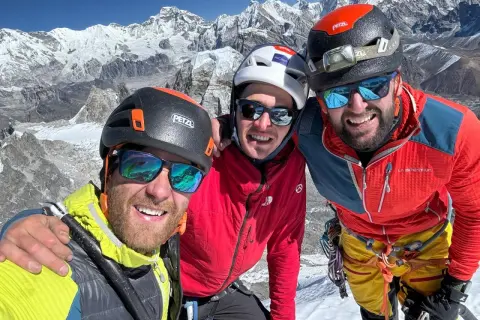 Trzech uśmiechniętych polskich wspinaczy w kaskach i okularach przeciwsłonecznych pozuje do selfie na tle ośnieżonych gór.