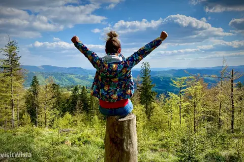 Radość na szlaku Wisła z dziećmi! Dziewczynka z podniesionymi rękami na pniu, podziwia malownicze widoki Beskidów.