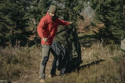 Mężczyzna w lesie składa namiot, przygotowując się do jego czyszczenia z pleśni.