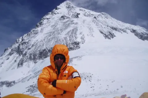 Alpinista w pomarańczowej kurtce na tle ośnieżonego szczytu. To może być jego wyczyn: mount everest bez tlenu.