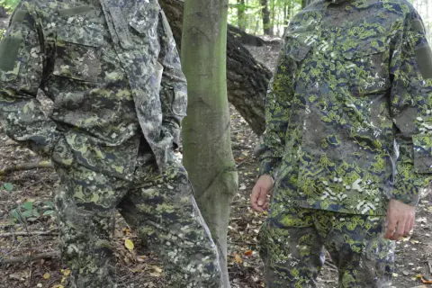 Dwie osoby w lesie w nowoczesnych kamuflażach wojskowych. Wzory kamuflażowe idealnie wtapiają się w otoczenie.