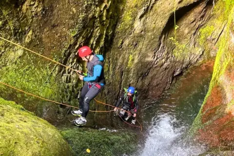 Dwóch mężczyzn w kaskach i piankach zjazdowych pokonuje wodospad w wąwozie. To właśnie jest canyoning!