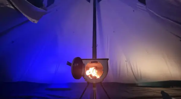 Piec w namiocie, płomienie tańczą w środku. Idealny sposób, jak ogrzać namiot zimową nocą.
