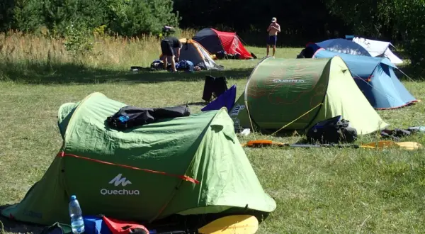 Zielony namiot Quechua, kilka innych rozstawionych na łące. Idealne miejsce, gdzie można rozbić namiot na dziko.