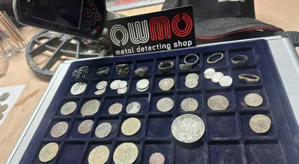 Oznaczenia na wykrywaczu metali i kolekcja monet oraz pierścionków znalezionych podczas poszukiwań.