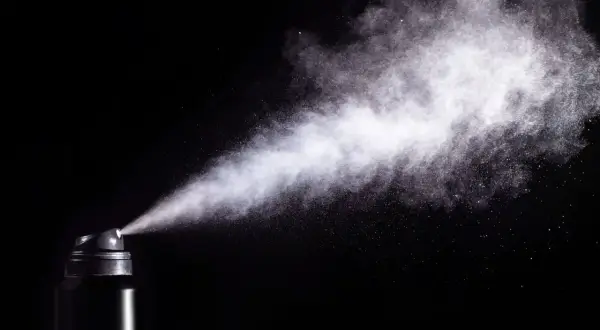 Chmura białego pyłu wydobywa się z czarnego aerozolu, ukazując potencjalne skutki gazu pieprzowego.