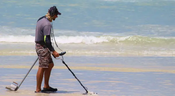 Mężczyzna z wykrywaczem metali na plaży. Czy wykrywacz metali jest legalny? Szuka skarbów w wodzie.