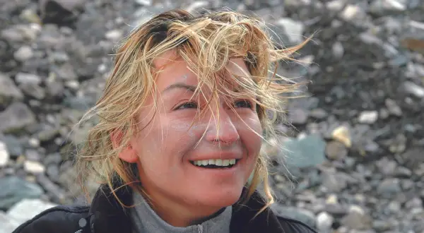Martyna Wojciechowska z wiatrem we włosach, uśmiechnięta, na tle kamienistego zbocza. Może to być wspomnienie z wyprawy na Mount Everest.