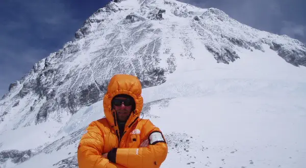 Alpinista w pomarańczowej kurtce na tle ośnieżonego szczytu. To może być jego wyczyn: mount everest bez tlenu.
