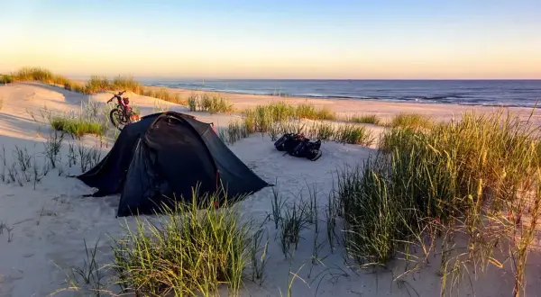 Namiot i rower na plaży, idealne miejsce na spanie na dziko. Wschód słońca nad morzem.