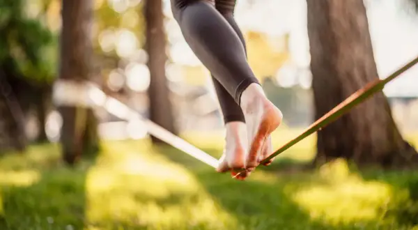 Chodzenie po taśmie to slackline. Widok na nogi balansujące na taśmie w parku, w promieniach słońca.