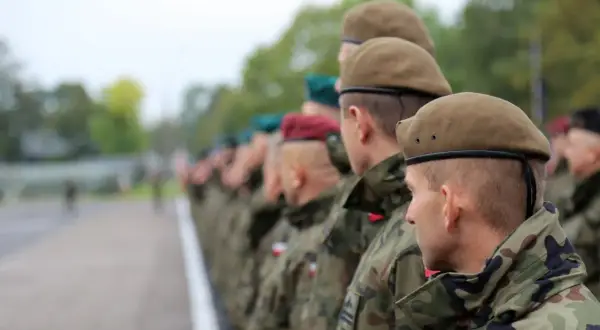 Żołnierze w kamuflażu i beretach stoją w szeregu. To kategoria d wojsko.