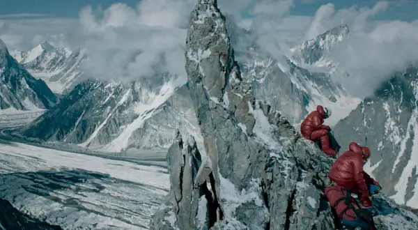 Wyprawa na Broad Peak 2013. Dwóch wspinaczy w czerwonych kurtkach odpoczywa na skalistym zboczu, podziwiając lodowce i ośnieżone szczyty.