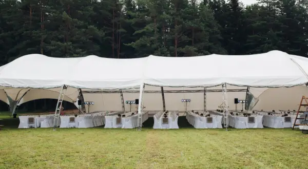 Duży biały namiot weselny z długimi stołami i krzesłami, gotowy na przyjęcie. Jak rozłożyć namiot? To proste, gdy masz taką konstrukcję!
