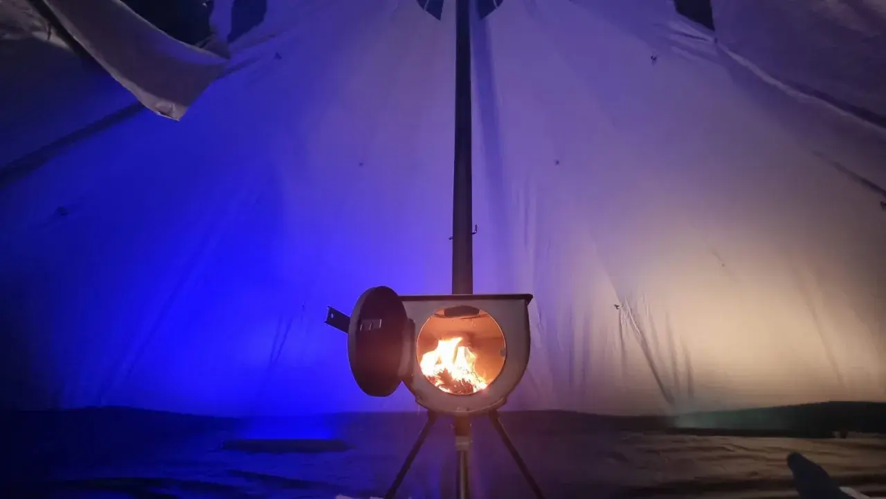 Piec w namiocie, płomienie tańczą w środku. Idealny sposób, jak ogrzać namiot zimową nocą.