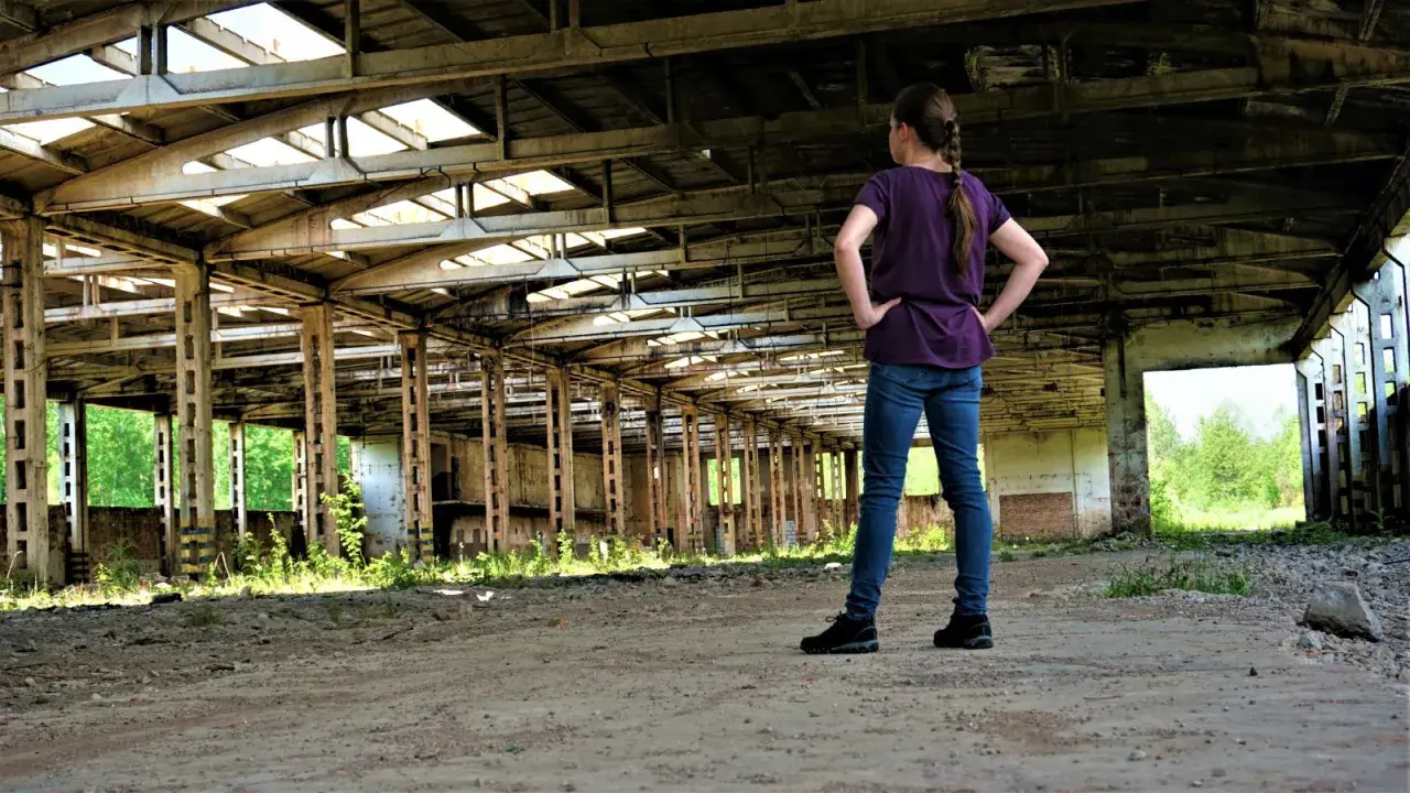Dziewczyna w zrujnowanej hali, zastanawia się, czy urbex jest legalny.