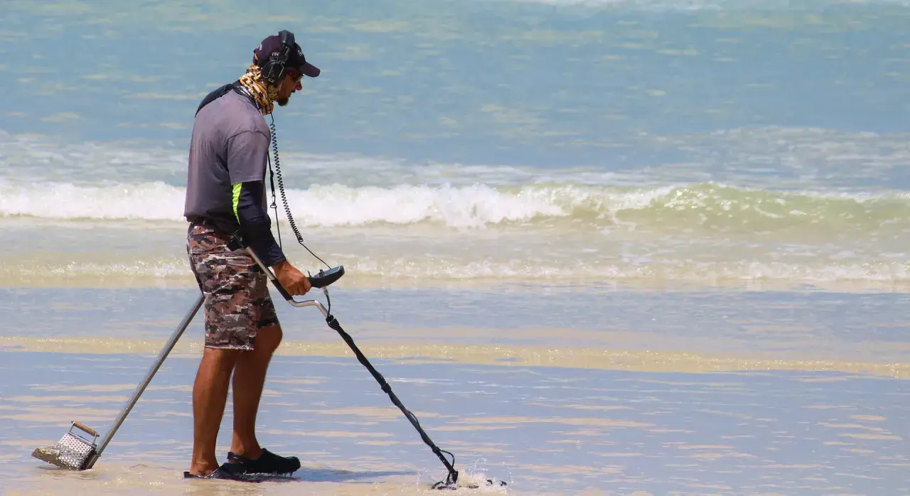 Mężczyzna z wykrywaczem metali na plaży. Czy wykrywacz metali jest legalny? Szuka skarbów w wodzie.