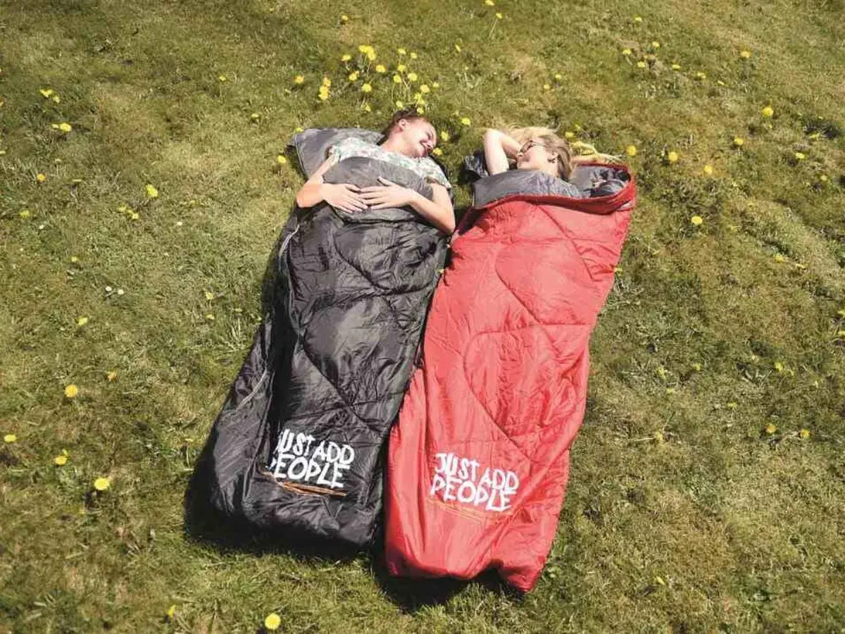 Dwie osoby leżą w śpiworach na trawie. Czarny śpiwór lewy czy prawy? Czerwony śpiwór też.