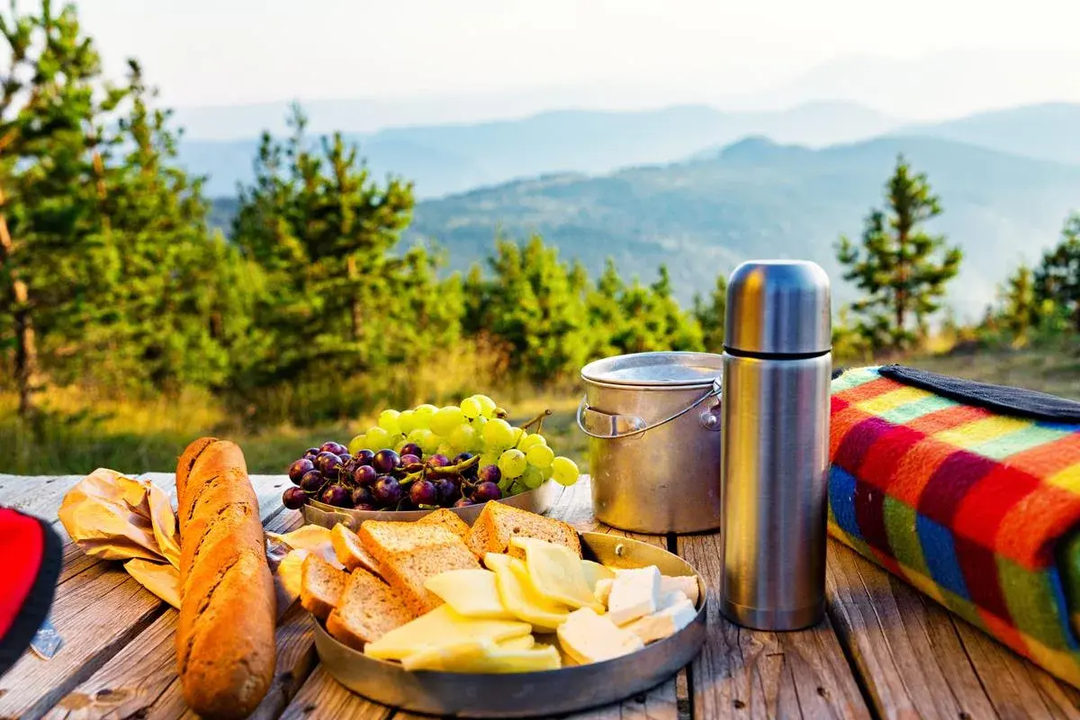Piknik w górach: chleb, ser, winogrona, termos i kolorowy koc. Idealne jedzenie, by cieszyć się widokiem.