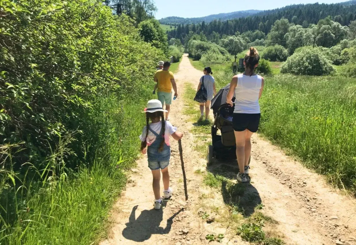 Rodzina spaceruje po górskiej ścieżce w Beskidach. Dziecko z patykiem idzie przodem, a za nim rodzice z wózkiem.